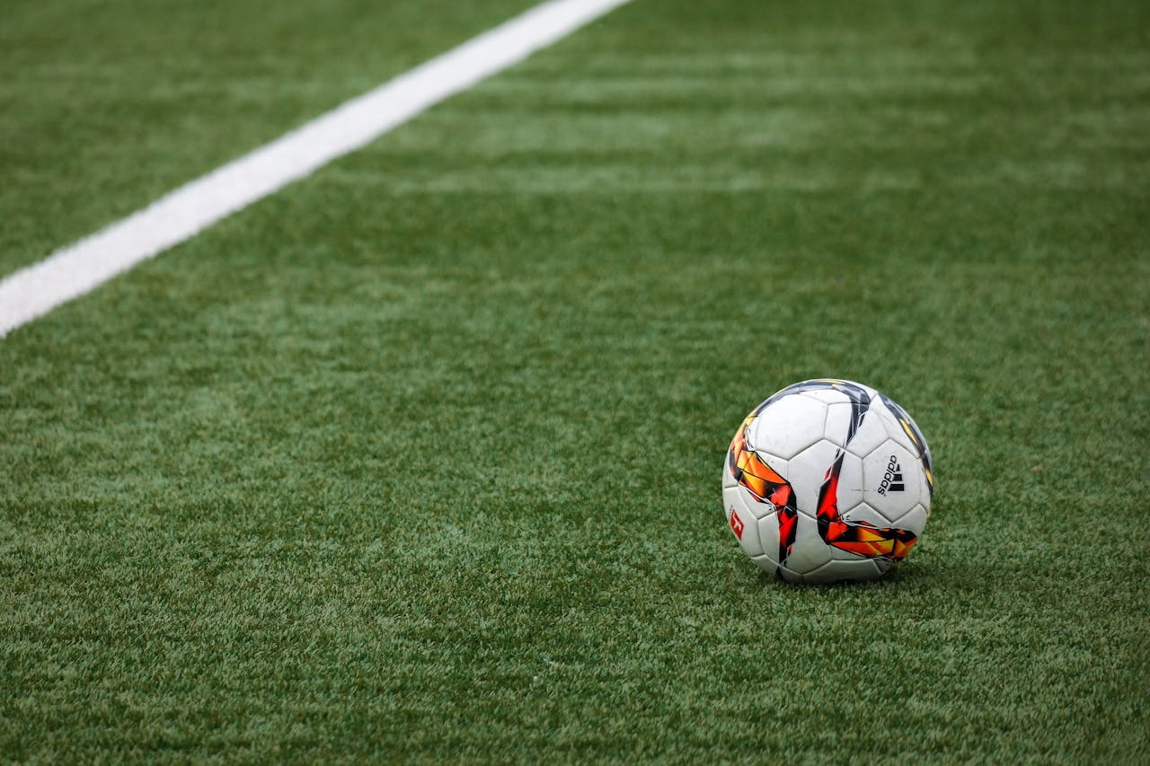 gallery-1 A vibrant soccer ball resting on a pristine grass field beside a white sideline.