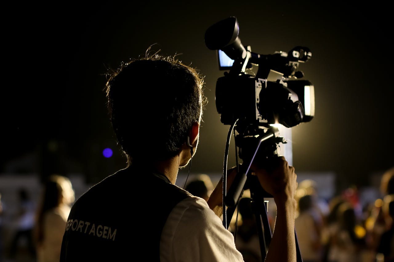 gallery-3 A cameraman filming an event outdoors at night with professional equipment, capturing the vibrant atmosphere.