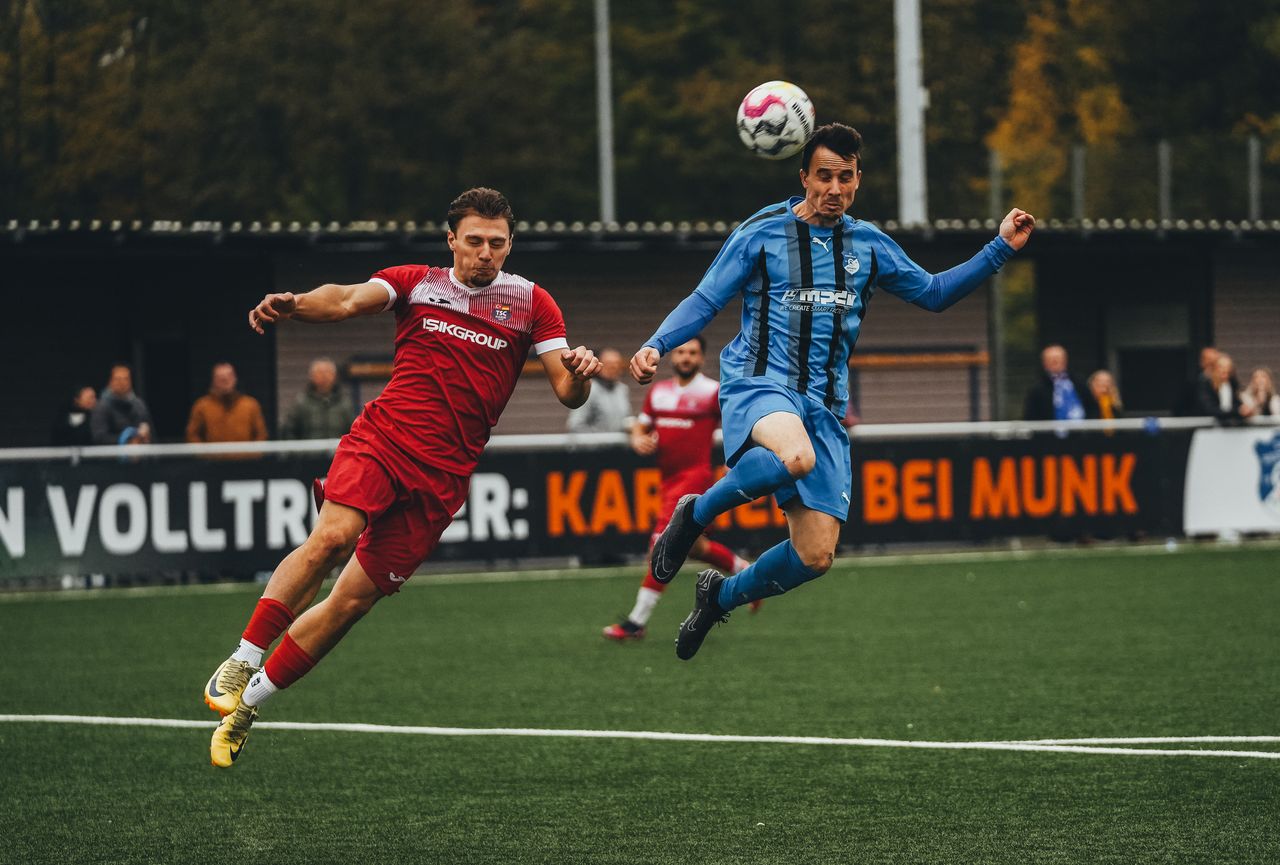 our-experience Dynamic photo of two soccer players mid-air during a competitive match.