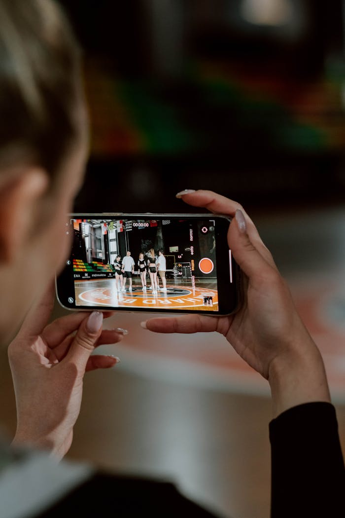 gallery-4 A person recording a cheerleading group with a smartphone during practice indoors.