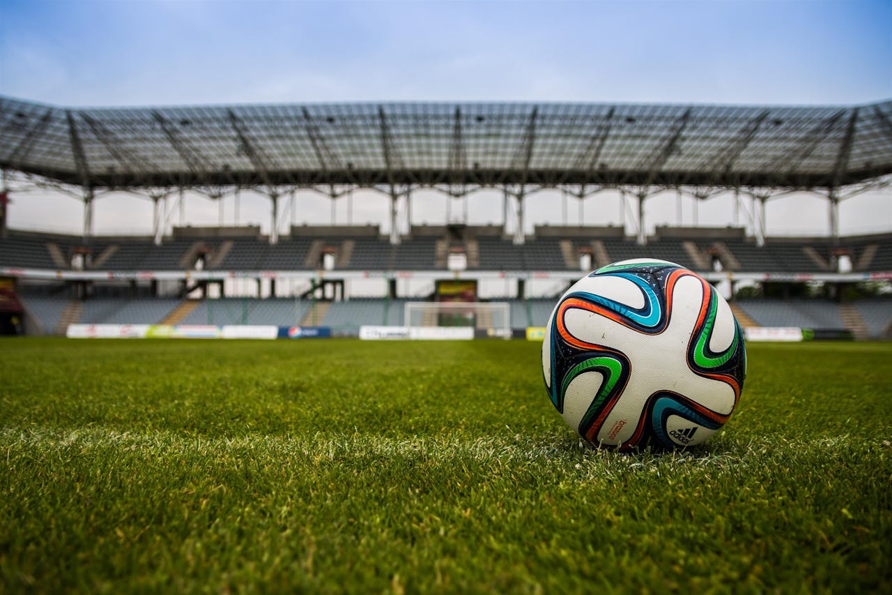 services-01 Close-up of a soccer ball on a lush grass field with an empty stadium in the background.